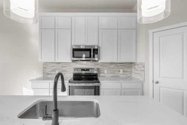 kitchen with pendant lighting, white cabinets, stainless steel appliances, tasteful backsplash, and sink