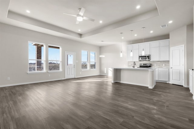 unfurnished living room featuring dark wood-type flooring, a raised ceiling, and ceiling fan