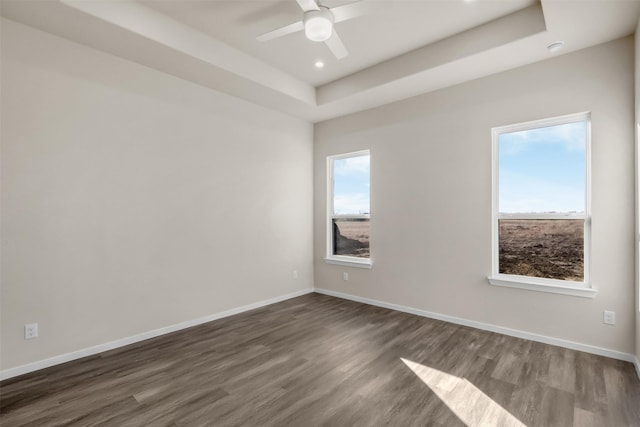 unfurnished room with ceiling fan, dark wood-type flooring, and a tray ceiling