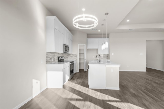 kitchen with white cabinets, stainless steel appliances, decorative backsplash, hanging light fixtures, and a center island with sink