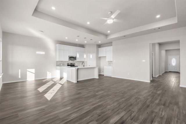 unfurnished living room featuring ceiling fan, dark wood-type flooring, and a tray ceiling