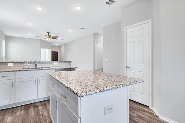 kitchen featuring dark hardwood / wood-style floors, a center island, sink, white cabinets, and light stone counters