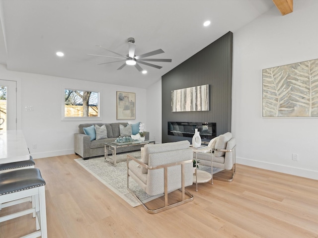 living room featuring ceiling fan, vaulted ceiling with beams, a fireplace, and light hardwood / wood-style floors