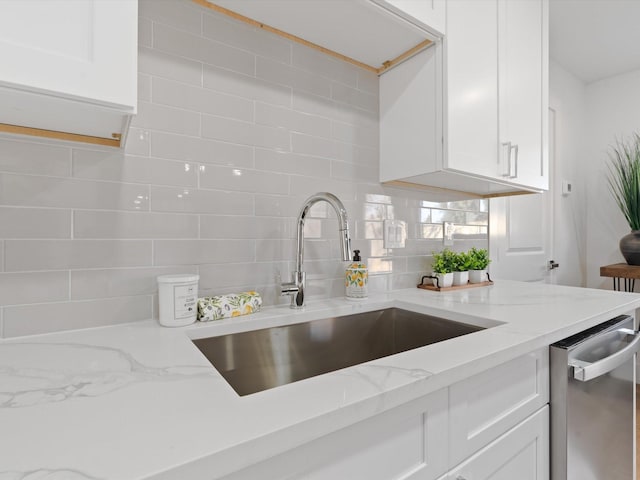 kitchen with decorative backsplash, light stone countertops, stainless steel dishwasher, white cabinets, and sink