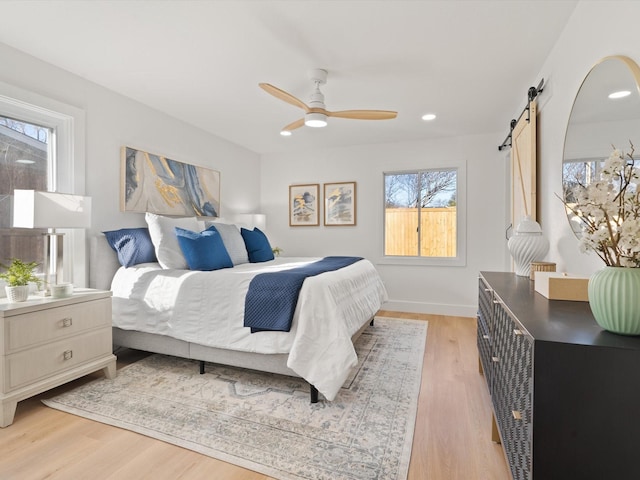 bedroom featuring ceiling fan, light hardwood / wood-style floors, a barn door, and multiple windows