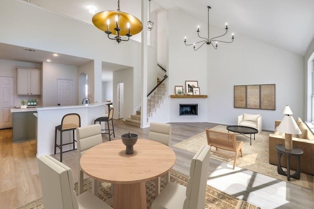 dining room featuring stairs, light wood-style floors, a fireplace, high vaulted ceiling, and a notable chandelier