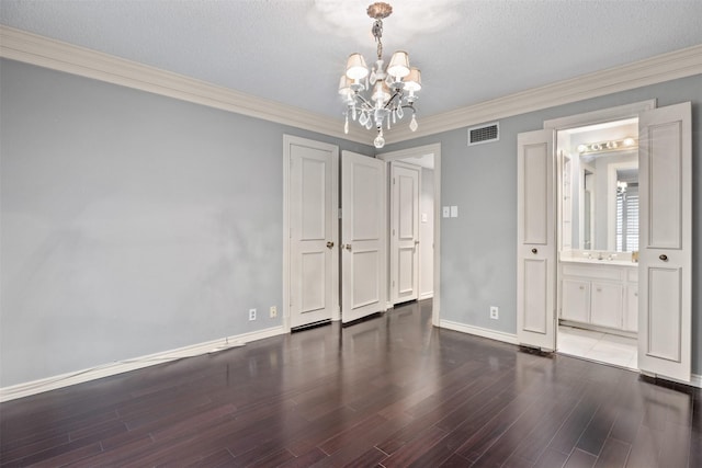 spare room with dark wood-type flooring, a textured ceiling, ornamental molding, and a chandelier