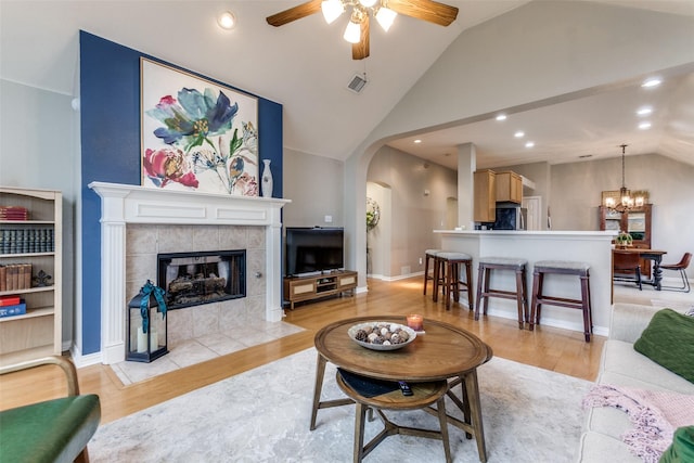 living room featuring a fireplace, ceiling fan with notable chandelier, high vaulted ceiling, and light wood-type flooring