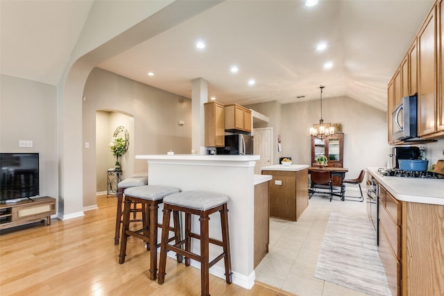 kitchen with lofted ceiling, a notable chandelier, a center island, pendant lighting, and appliances with stainless steel finishes