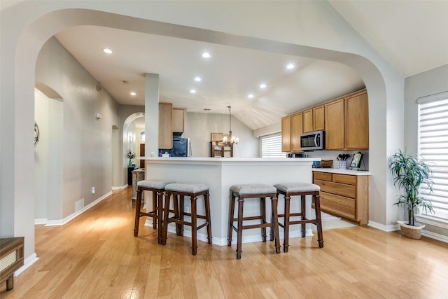 kitchen with a center island, lofted ceiling, hanging light fixtures, light hardwood / wood-style flooring, and a breakfast bar area