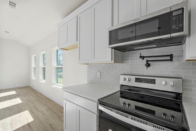 kitchen with stainless steel appliances, lofted ceiling, backsplash, and white cabinetry