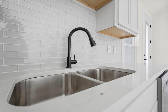 interior details with backsplash, sink, and white cabinetry