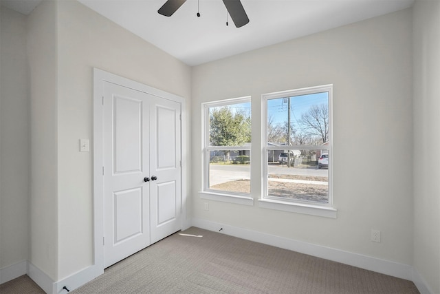 unfurnished bedroom with light carpet, ceiling fan, a closet, and multiple windows