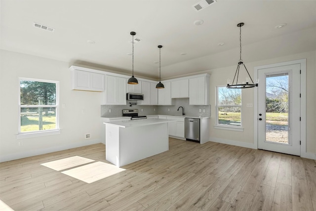 kitchen featuring appliances with stainless steel finishes, white cabinetry, hanging light fixtures, and a center island