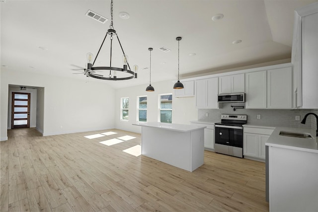 kitchen featuring a kitchen island, sink, white cabinetry, hanging light fixtures, and stainless steel appliances