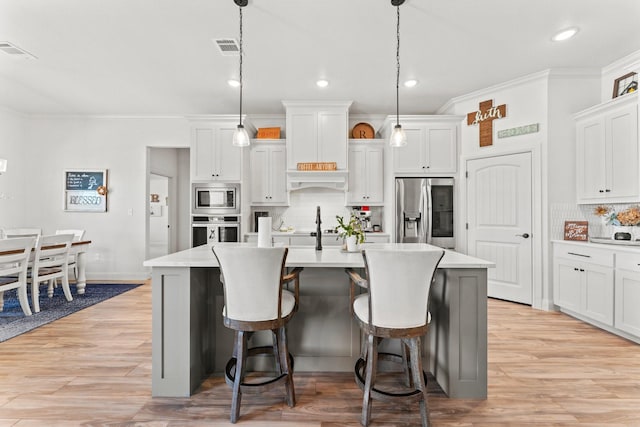 kitchen featuring white cabinetry, stainless steel appliances, a center island with sink, and hanging light fixtures