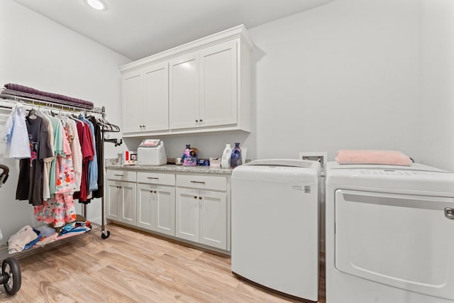 clothes washing area with washer and clothes dryer, light hardwood / wood-style flooring, and cabinets