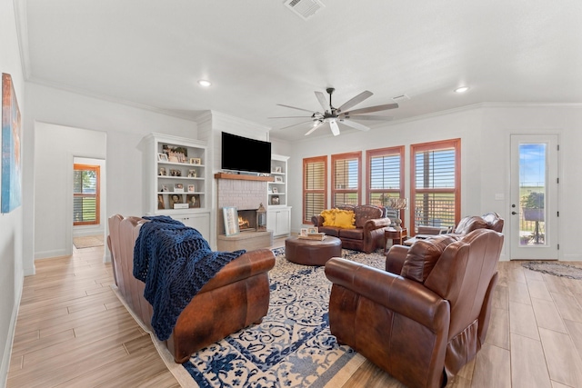 living room featuring built in shelves, a fireplace, ceiling fan, light hardwood / wood-style flooring, and crown molding