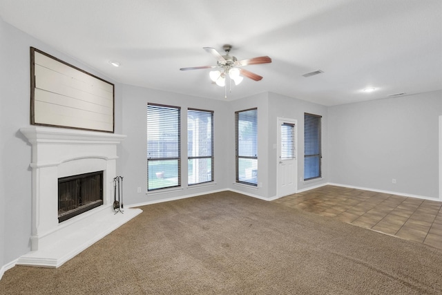 unfurnished living room with a ceiling fan, a fireplace with raised hearth, visible vents, and carpet floors