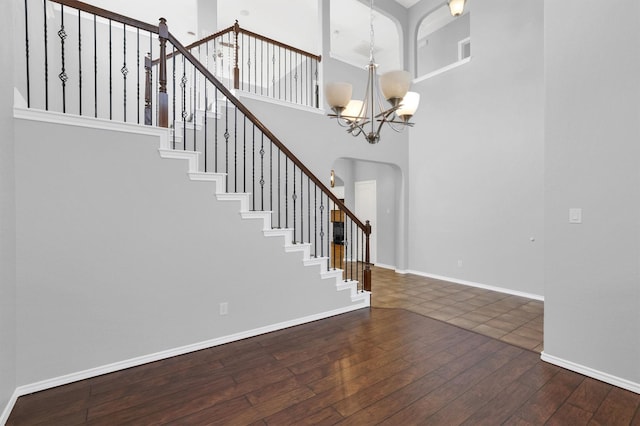 foyer with baseboards, dark wood finished floors, an inviting chandelier, arched walkways, and stairs