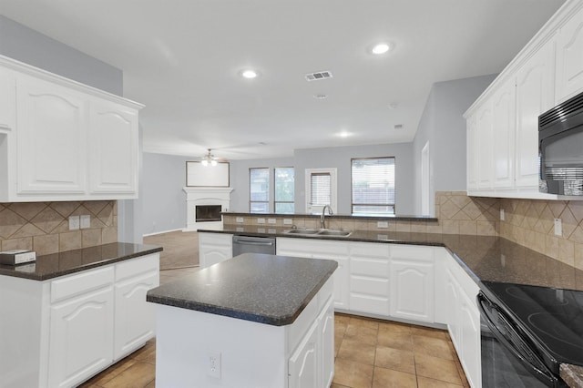 kitchen with visible vents, a peninsula, a fireplace with raised hearth, a sink, and black appliances