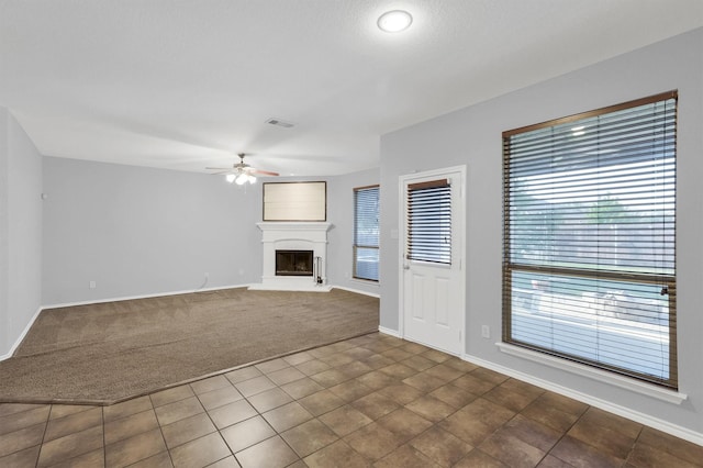 unfurnished living room featuring dark colored carpet, baseboards, a fireplace with raised hearth, and a ceiling fan