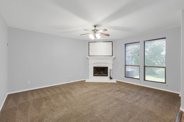 unfurnished living room with carpet flooring, a fireplace with raised hearth, baseboards, and ceiling fan