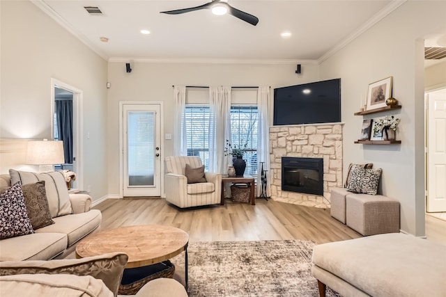 living room featuring crown molding, ceiling fan, a stone fireplace, and light hardwood / wood-style floors