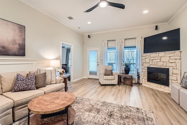 living room with ornamental molding, a stone fireplace, ceiling fan, and light hardwood / wood-style flooring