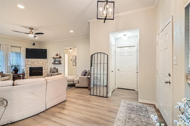 living room with crown molding, a stone fireplace, light hardwood / wood-style floors, and ceiling fan with notable chandelier