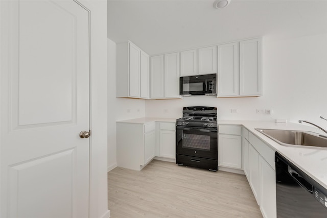 kitchen with black appliances, sink, white cabinetry, and light hardwood / wood-style flooring