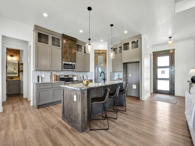 kitchen with appliances with stainless steel finishes, decorative light fixtures, backsplash, light stone counters, and a center island with sink