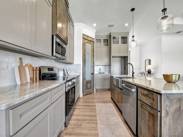 kitchen featuring light stone counters, an island with sink, pendant lighting, and appliances with stainless steel finishes