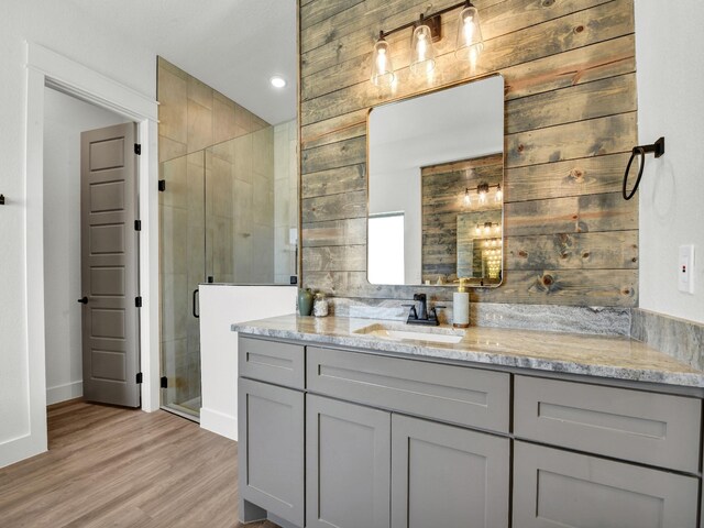 bathroom with wood walls, hardwood / wood-style flooring, walk in shower, and vanity