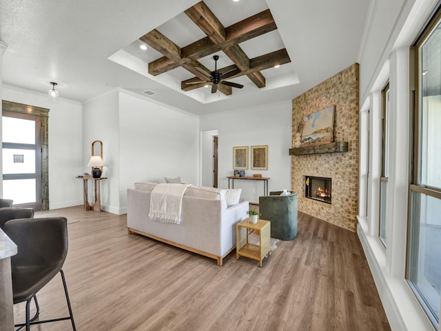 living room featuring crown molding, wood-type flooring, coffered ceiling, a large fireplace, and beam ceiling