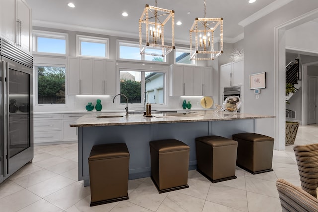 kitchen with white cabinets, light stone countertops, an island with sink, and high quality fridge