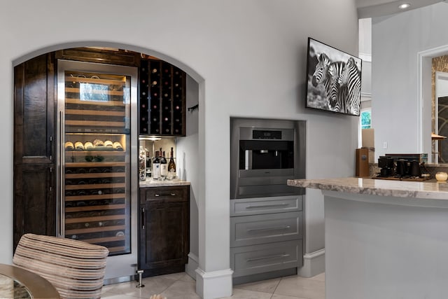 bar with gray cabinetry, oven, light tile patterned flooring, wine cooler, and light stone countertops