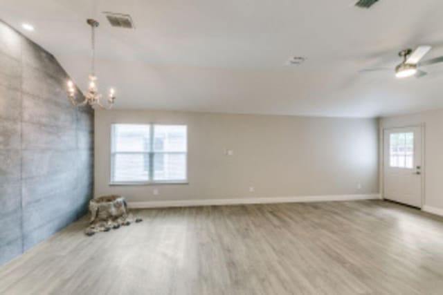 empty room featuring ceiling fan with notable chandelier and hardwood / wood-style floors