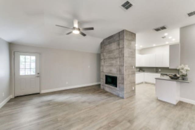 unfurnished living room featuring light hardwood / wood-style floors, a large fireplace, ceiling fan, and vaulted ceiling