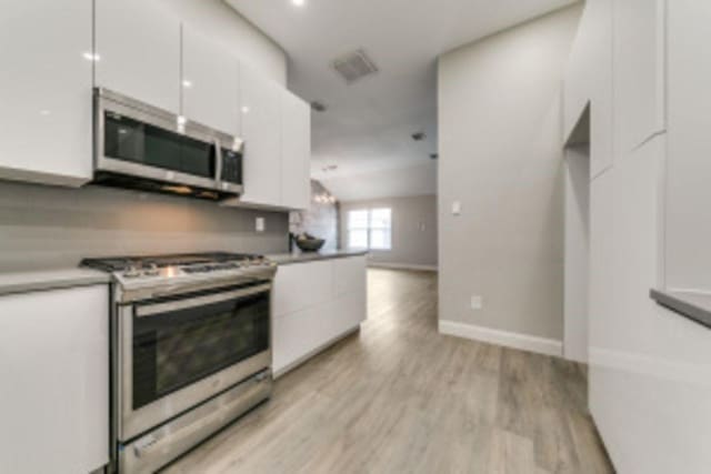 kitchen featuring vaulted ceiling, appliances with stainless steel finishes, light hardwood / wood-style floors, and white cabinetry