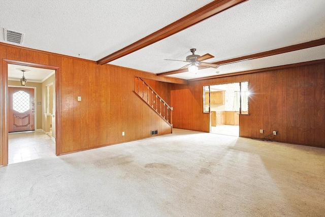 unfurnished living room with carpet floors, ceiling fan, beam ceiling, wooden walls, and a textured ceiling