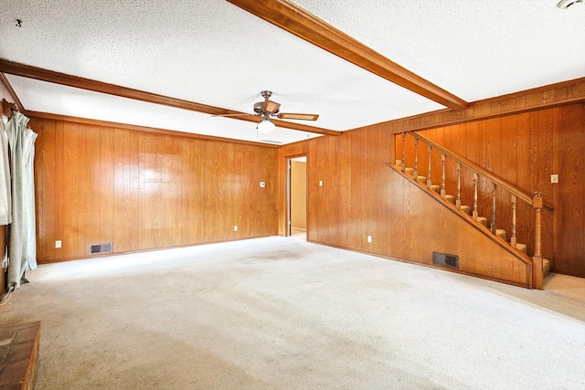 unfurnished living room featuring ceiling fan, light colored carpet, beamed ceiling, wooden walls, and a textured ceiling