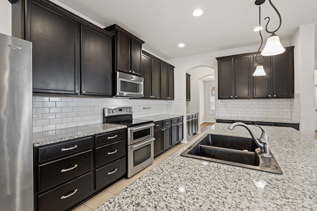 kitchen featuring sink, decorative light fixtures, dark brown cabinets, stainless steel appliances, and backsplash