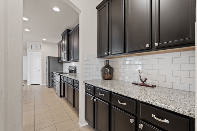 kitchen with light tile patterned flooring, appliances with stainless steel finishes, light stone counters, and backsplash