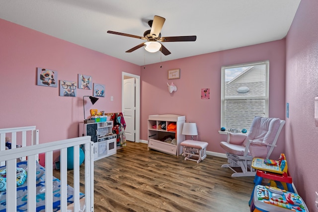 bedroom featuring a crib, ceiling fan, and dark hardwood / wood-style flooring