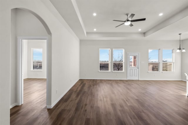 unfurnished living room with a raised ceiling, dark wood-type flooring, and ceiling fan with notable chandelier