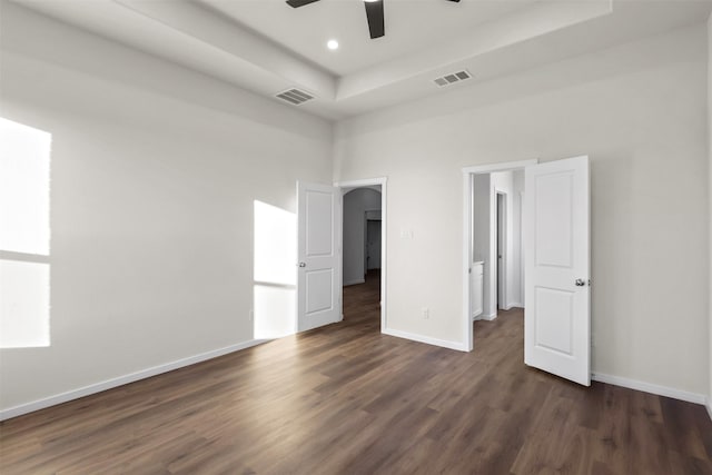 unfurnished bedroom featuring ceiling fan, dark hardwood / wood-style flooring, a towering ceiling, and a raised ceiling