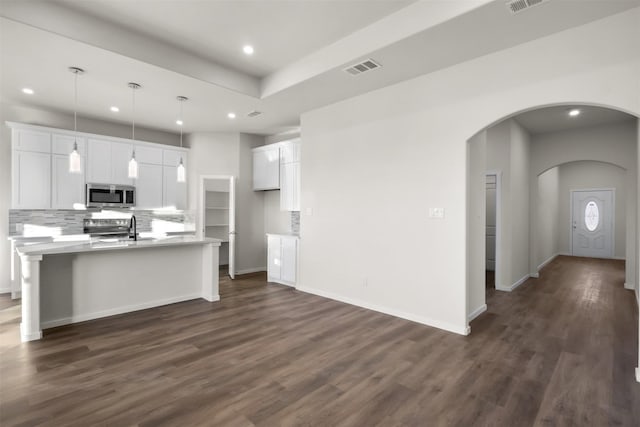 kitchen featuring an island with sink, stainless steel appliances, backsplash, decorative light fixtures, and white cabinets