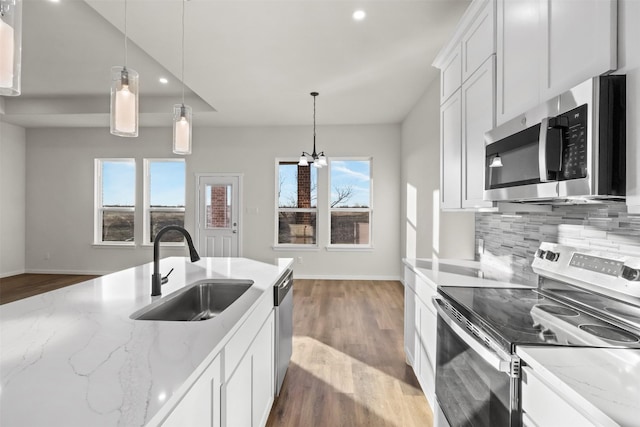 kitchen featuring appliances with stainless steel finishes, decorative light fixtures, light stone countertops, white cabinets, and sink