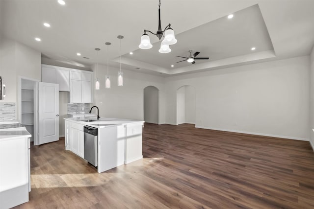 kitchen featuring decorative backsplash, white cabinets, a tray ceiling, and a center island with sink